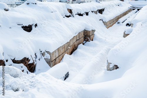 A pit with concrete walls for laying pipes of city communications  replacement of old heating networks with new pipes  winter construction work under snow.