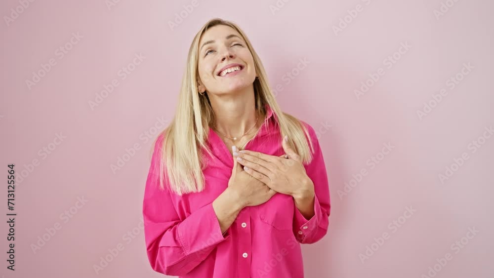 Cheerful young blonde woman, standing over a pink isolated background, proudly places hands on chest, expressing a feeling of gratitude. portrait of a healthy, confident female smiling. Cheerful young blonde woman, standing over a pink isolated background, proudly places hands on chest, expressing a feeling of gratitude. portrait of a healthy, confident female smiling.