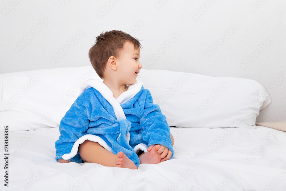 Baby in blue bathrobe, after bath, sitting on bed. Emotions, copy space. Baby in blue bathrobe, after bath, sitting on bed. Emotions, copy space.