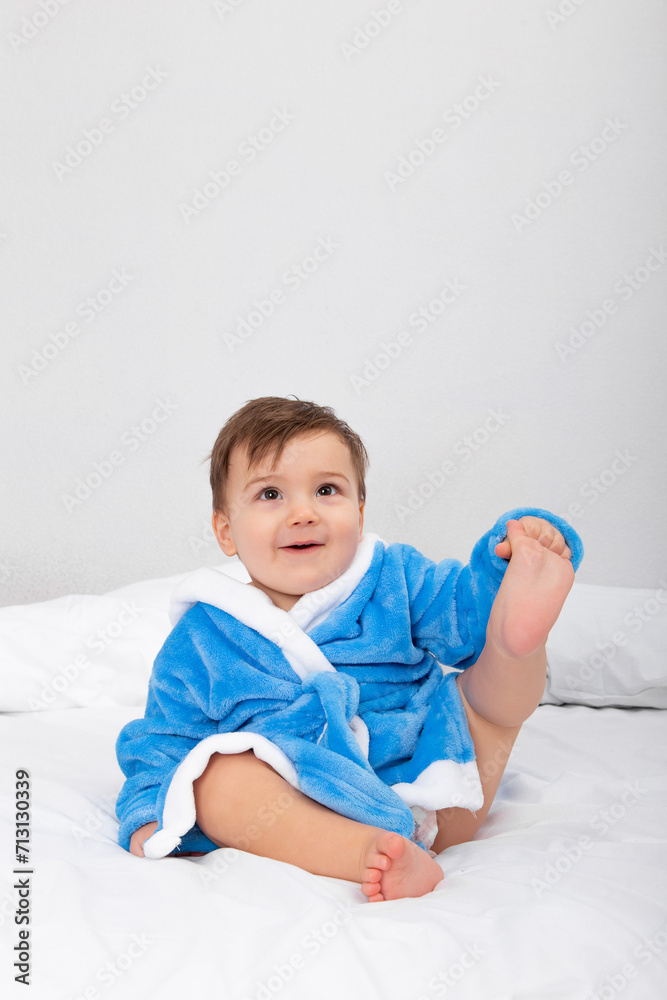 Baby in blue bathrobe, after bath, sitting on bed. Emotions, copy space. Baby in blue bathrobe, after bath, sitting on bed. Emotions, copy space.
