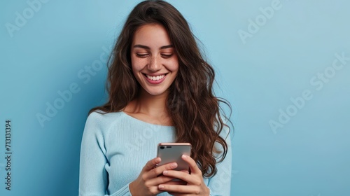 oung adult smiling happy pretty latin woman holding mobile phone looking at smartphone, typing message doing ecommerce shopping on cell, using trendy apps on cellphone isolated on blue background
