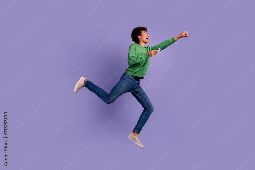 Full length photo of excited cool guy wear green pullover running sale modern gadget empty space isolated purple color background