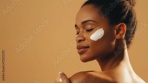 Young Black African woman applying moisturizing nutritive sunscreen lotion cream on body after shower on brown background. photo
