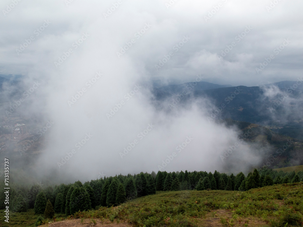 A serene, misty landscape with green, rolling hills and distant mountains enveloped by clouds, creating a mystical atmosphere