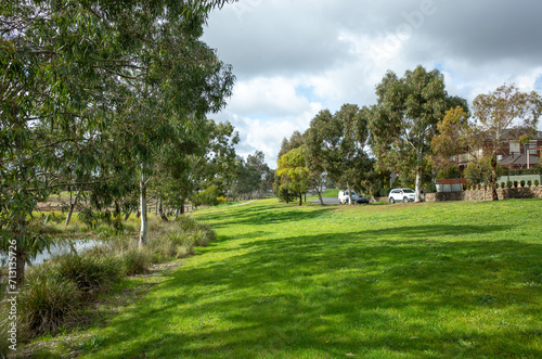Background texture of a large lawn with healthy and green grass near some suburban houses. A local park in a Melbourne’s suburb with open space, plants and a water pond. Copy space for your design.