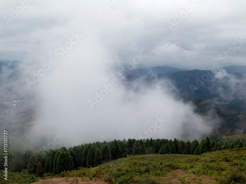 A serene, misty landscape with green, rolling hills and distant mountains enveloped by clouds, creating a mystical atmosphere
