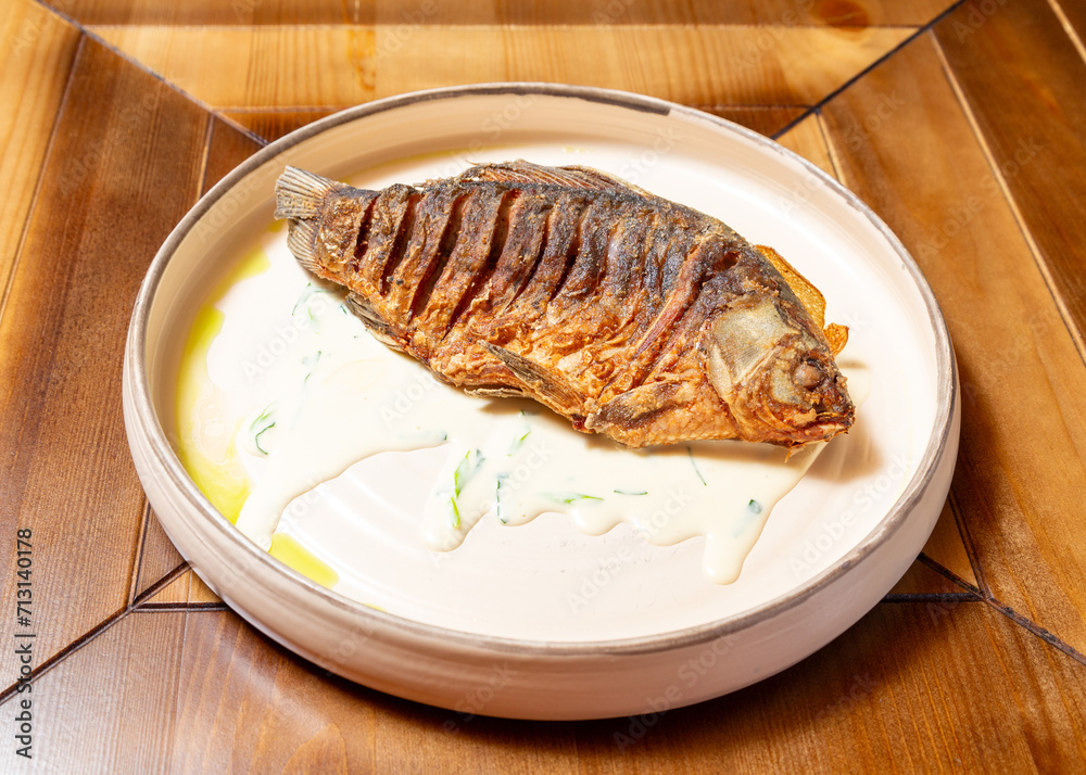 Whole fried fish on a plate. On a wooden table. Whole fried fish on a plate. On a wooden table.