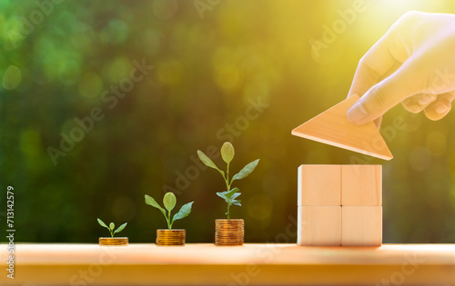 hand putting triangle wooden block to assemble complete as one, Property investment and house mortgage financial real estate concept, coin stack and grow plant, garden background, morning light. photo