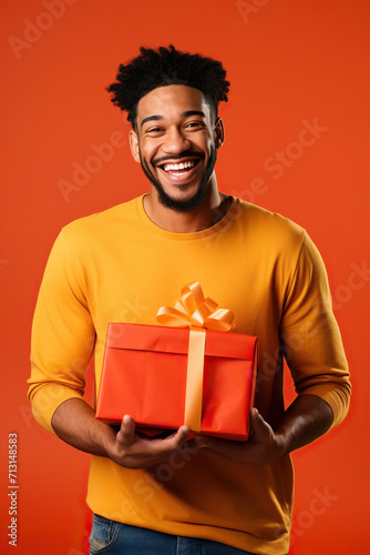 Young smiling happy African American man wearing t-shirt casual clothes hold present box with gift ribbon bow looking aside on area isolated on orange red color background studio portrait. © AI_images