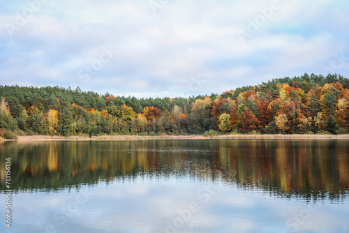 Autumn colored forest reflected in the surface of the lake water. Jesień kolorowy las odbijający się w tafli wody jeziora.