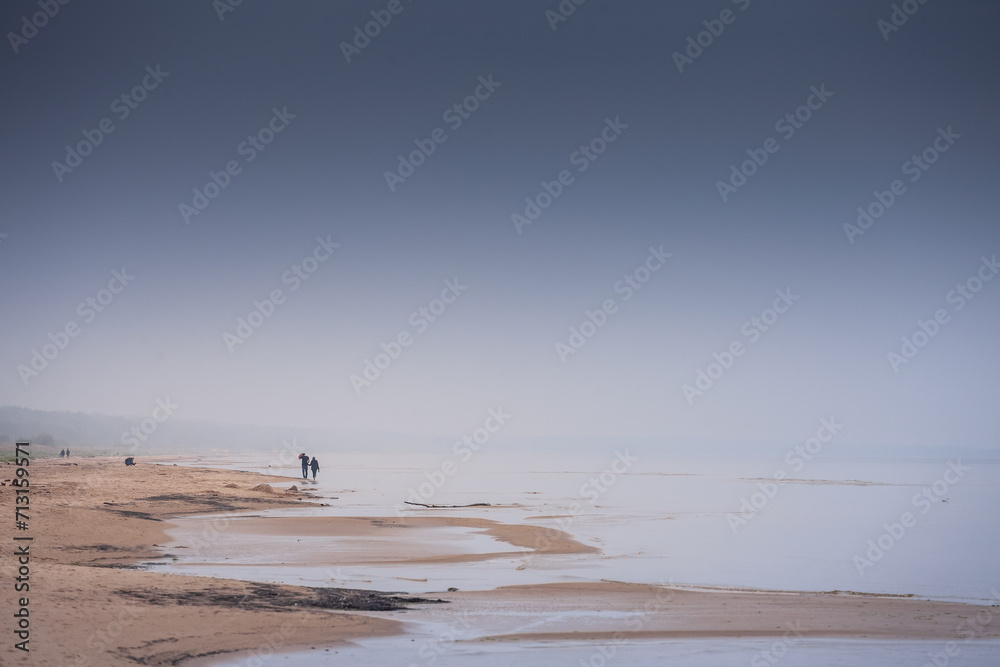 Panorama of the Garciems beach with unrecognizable people walking (Garciema Pludmale) in Latvia, on the baltic sea, on rainy foggy cloudy afternoon. Garciems is a sea resort of Latvia in baltic states