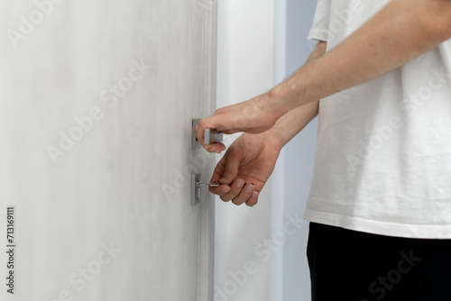 A close-up view of a persons hand as they insert a silver key into the keyhole of a contemporary door, ready to unlock it.