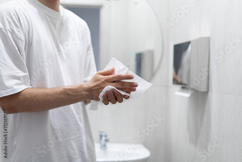 A person is captured drying their hands using a paper towel in the clean and well-lit confines of a modern bathroom setting.