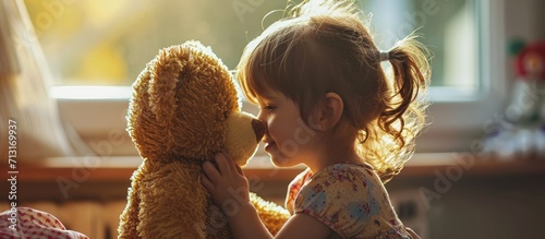 Adorable little girl enjoying her childhood at home with her favourite toy a cute teddy bear She touches noses with the stuffed animal enjoying her leisure time and the innocence of childhood photo
