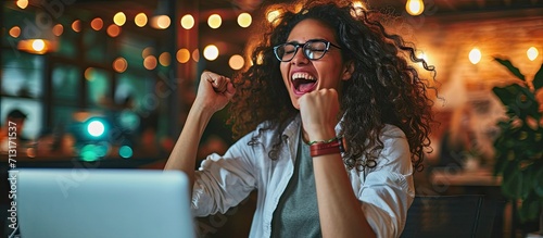 Hispanic business woman celebrating victory success employee with curly hair inside office reading good news using laptop at work inside office holding hand up and happy triumph gesture