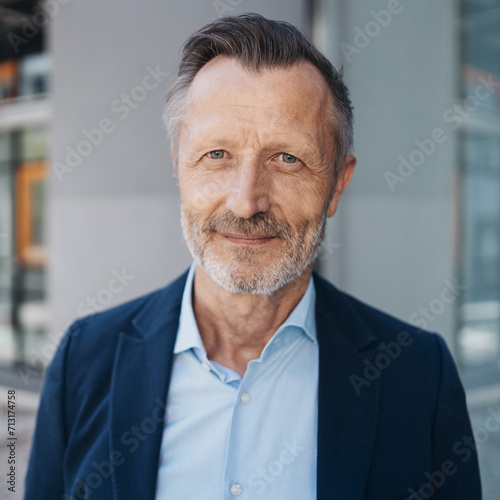Obraz na płótnie Confident 55-Year-Old Businessman in Modern Shirt, Standing Before Sleek Glass and Concrete Wall, Gazing Relaxed into the Camera