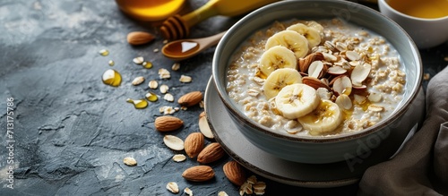 Bowl of oatmeal porridge with sliced banana almonds sunflower seeds and honey Cup of green tea jar of honey and ripe bananas on side. Copy space image. Place for adding text photo