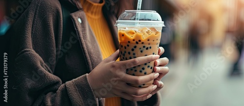 Bubble milk tea fever theme female hands holding and clinking transparent disposable plastic glass with dome lid contained iced bubble or boba milk tea with black jumbo plastic drinking straw photo