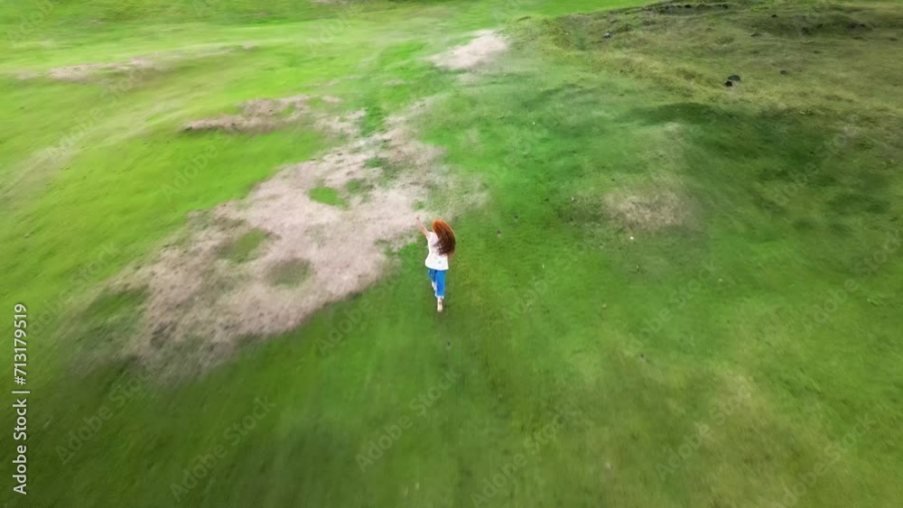 Girl with red hair runs across a green field, top view, filmed by drone 