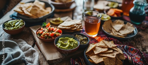 A tablecloth with geometric patterns and elegant leaves decorates the table where two bowls of hummus and guacamole are served with whole wheat toast and breadsticks A healthy and delicious sna photo