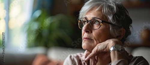 Stressed senior retired woman touching forehead looking away feeling doubtful about decision Unhappy thoughtful middle aged lady sitting on couch worrying about personal problems alone at home photo