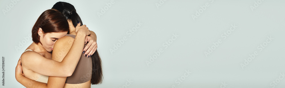 young woman with closed eyes embracing her friend while showing support on grey background, banner - obrazy, fototapety, plakaty 