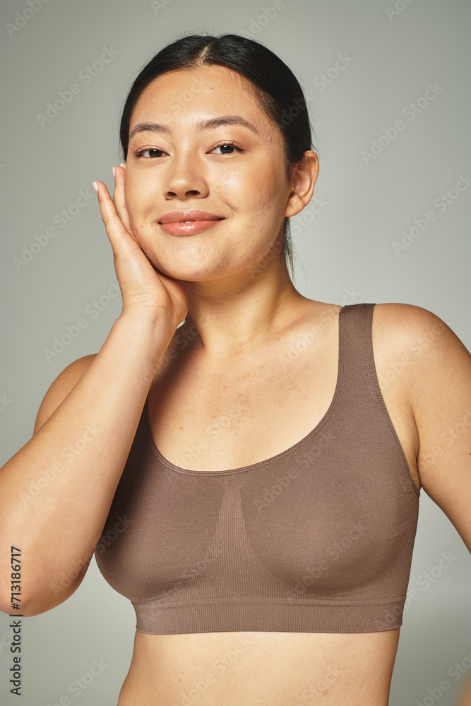 pretty asian woman in brown top touching her face on grey background, skin care and body positive pretty asian woman in brown top touching her face on grey background, skin care and body positive