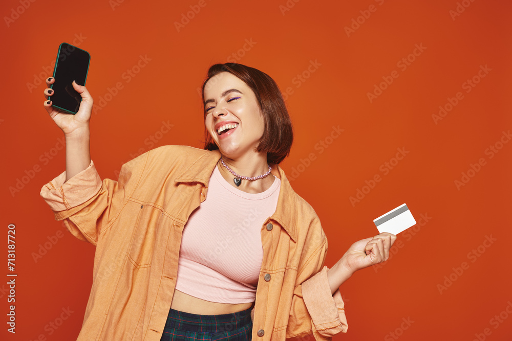 young happy woman holding smartphone and credit card on orange background, ecommerce concept young happy woman holding smartphone and credit card on orange background, ecommerce concept