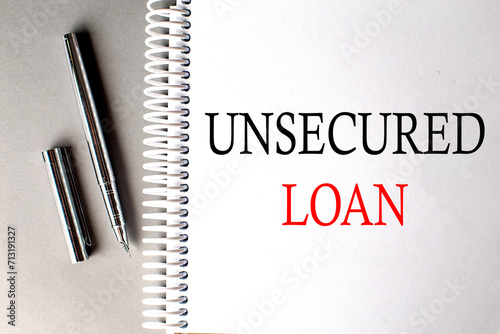 UNSECURED LOAN text on a notebook with pen on grey background