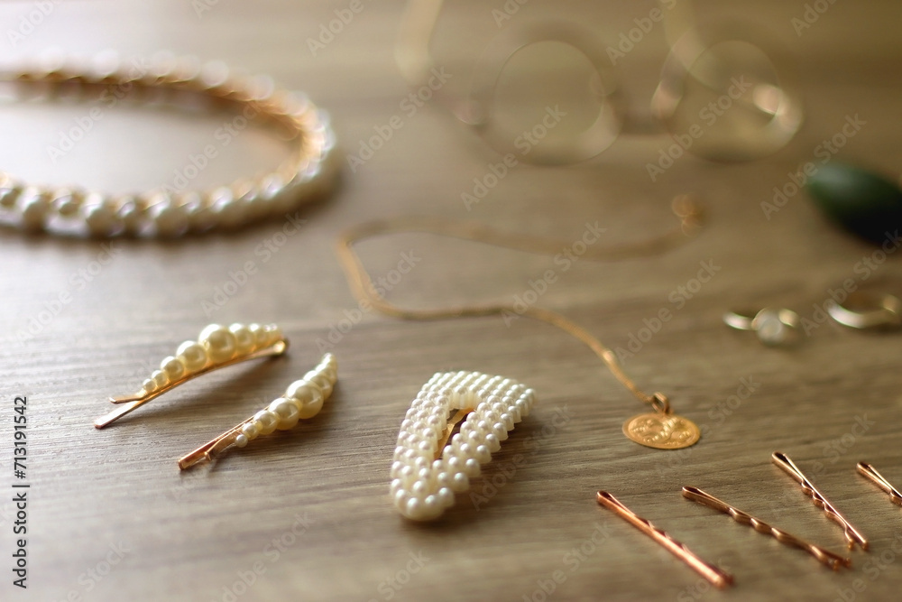 Pearl headband and barrette, golden eyeglasses, gold necklace, earrings and rings, jade face roller and hair pins on wooden background. Various elegant gold accessories. Selective focus.