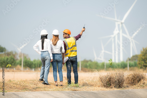 Back view of group engineers and architects on construction site with wind turbines in background