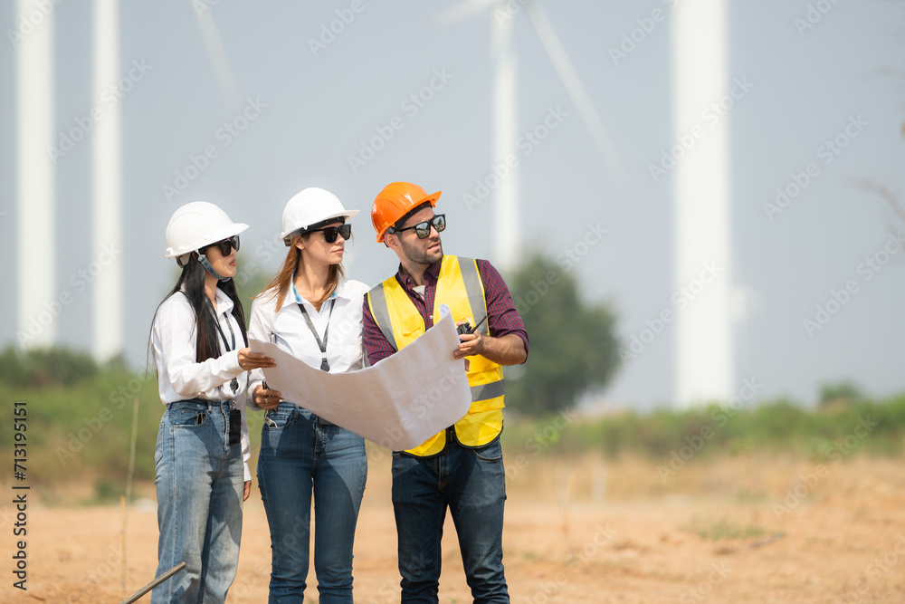 Group of engineers and architects on construction site with wind turbines in background Group of engineers and architects on construction site with wind turbines in background