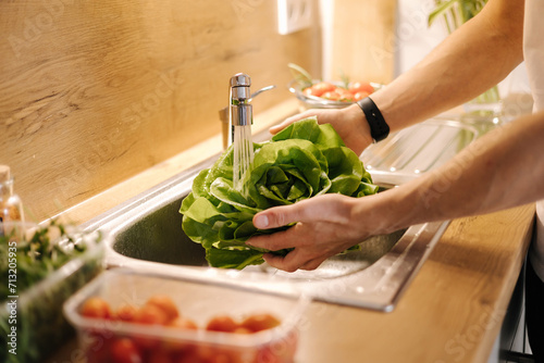 Man washing organic green salad Romano in kitchen. Lettuce leaves with water drops