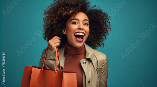 Excited young african american woman holding a bag in the hand isolated on sea blue background, positive emotion, sale discount shopping concept, person with a bag, having fun shopping photo