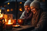 As the warm flame of the candle flickers in the cold winter air, a man and woman sit at a table with cups of tea, their faces glowing with smiles as they find comfort in each other's company indoors