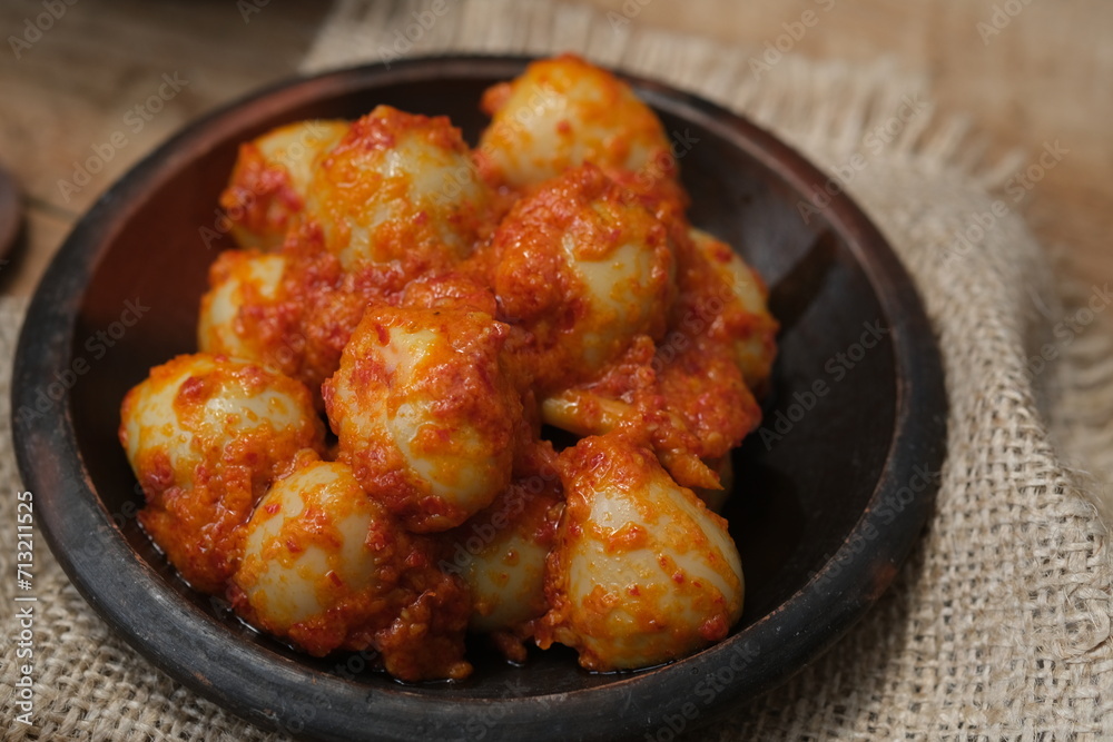 Telur Balado Tomat or Spicy Egg is traditional popular Indonesian food made from boiled egg with tomato and chili paste or sambal, served in earthenware plate on wooden table. Garlic, tomato, chilli. Telur Balado Tomat or Spicy Egg is traditional popular Indonesian food made from boiled egg with tomato and chili paste or sambal, served in earthenware plate on wooden table. Garlic, tomato, chilli.