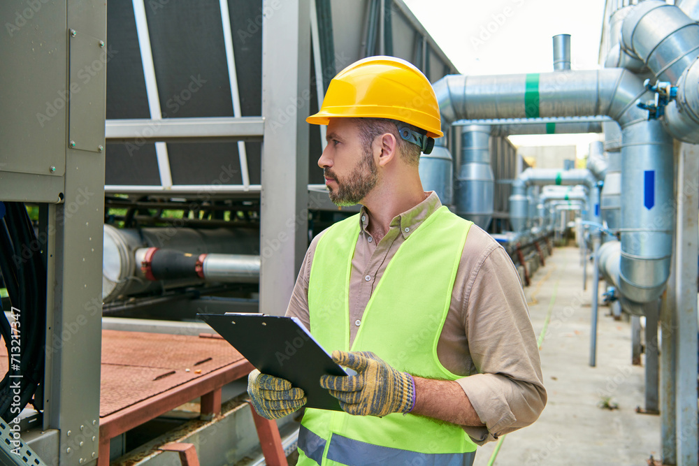 good looking focused technician in safety helmet holding clipboard and looking away, data center good looking focused technician in safety helmet holding clipboard and looking away, data center