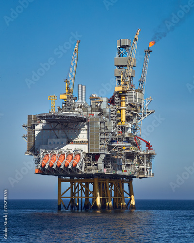 Offshore oil and gas jackup rig in the ocean during clear, bright day, with blue sky and calm water.