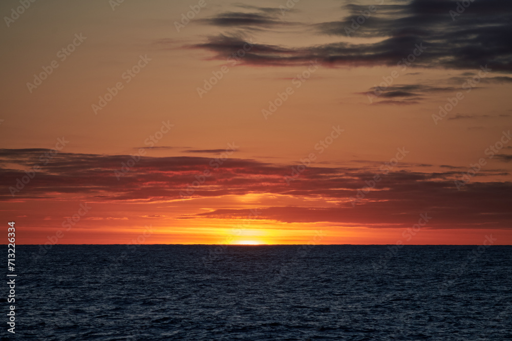 Fototapeta premium Dramatic colourful dark sky in the sea with waves on the water and sun on the horizon.