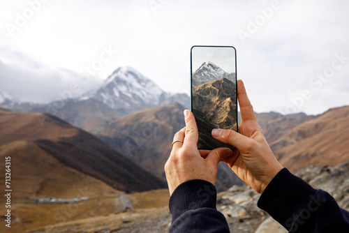 Foto A hand holds a smartphone capturing the breathtaking view of a majestic mountain landscape