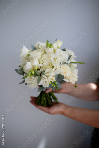 Bouquet of white flowers in female hands on a gray background. The concept of selling bouquets for the holiday.