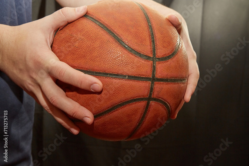 Two hands holding a basketball in close-up on a dark background, playing basketball, street basketball