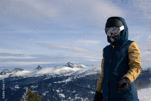 Woman in ski or snowboard equipment against backdrop of rocky mountains. Warm jacket, gloves, ski goggles and helmet