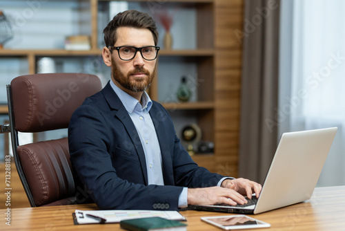 Focused mature man in stylish office working on laptop. Business professional, lawyer, or banker in a home environment.