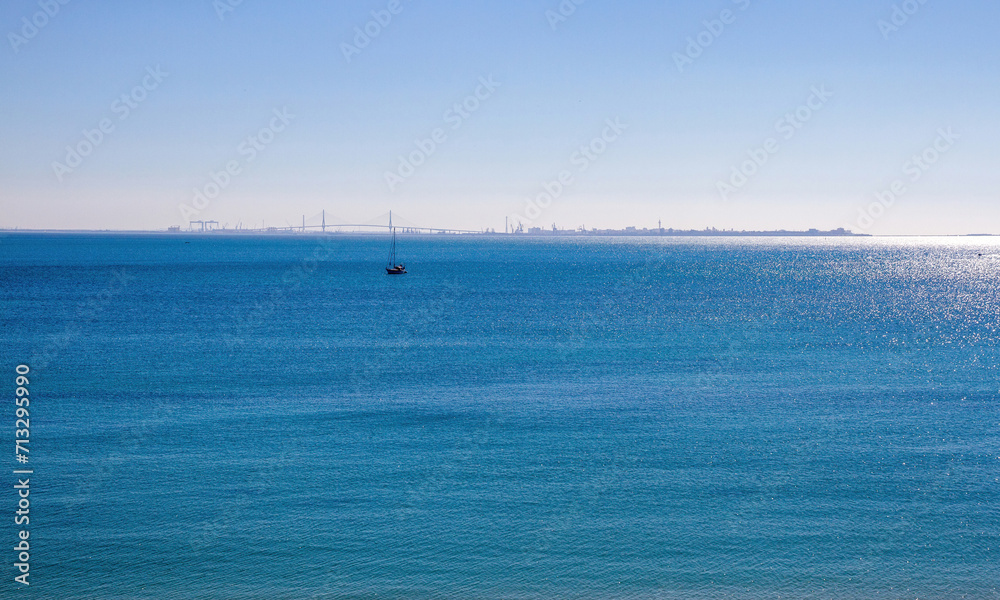 View on the skyline of Cadiz from Rota with the bridge and a boat in the sea, Andalusia, Spain 