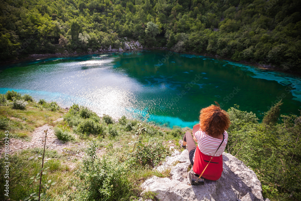 Curly Hair Caucasian Adult Woman Sitting on a Rock and Looking at View of the Beautiful Alpine Lake of Cornino - Italy