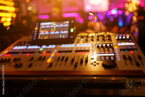 Modern sound mixer console with colorful buttons and sliders, set against the backdrop of a live music venue