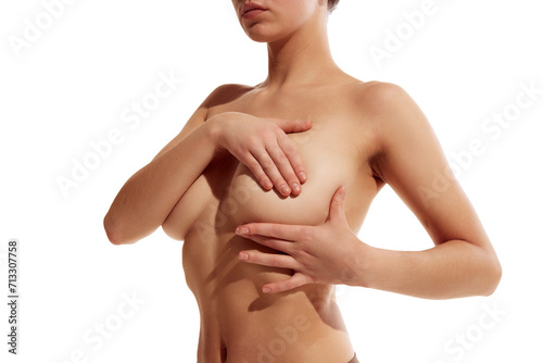 Cropped portrait of naked young lady with perfect curves covering her beast with hand against white studio background. Concept of beauty, body and skin care, health, plastic surgery