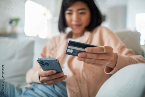 Smiling young adult woman using credit card on smartphone at home photo
