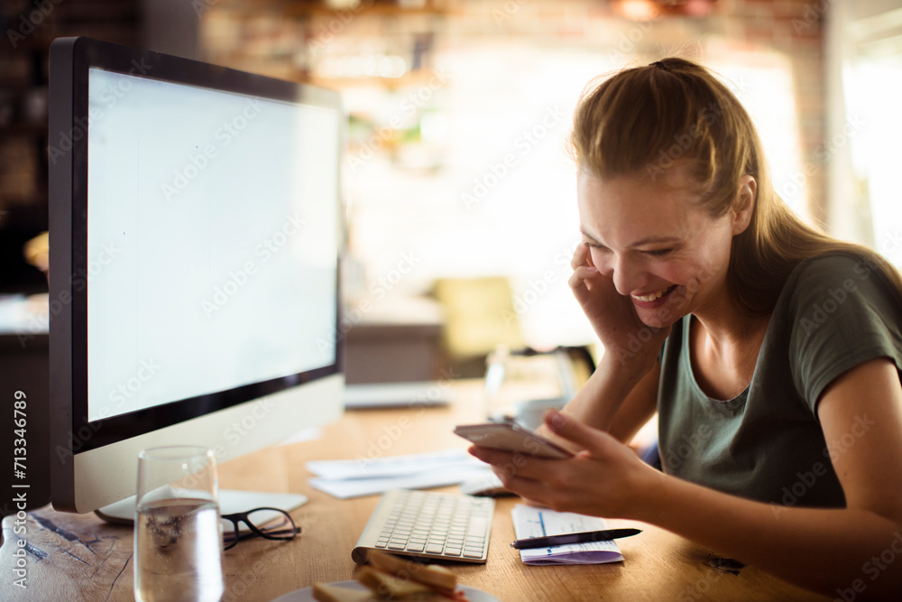 Woman smiling and using smartphone while having breakfast at home computer Woman smiling and using smartphone while having breakfast at home computer